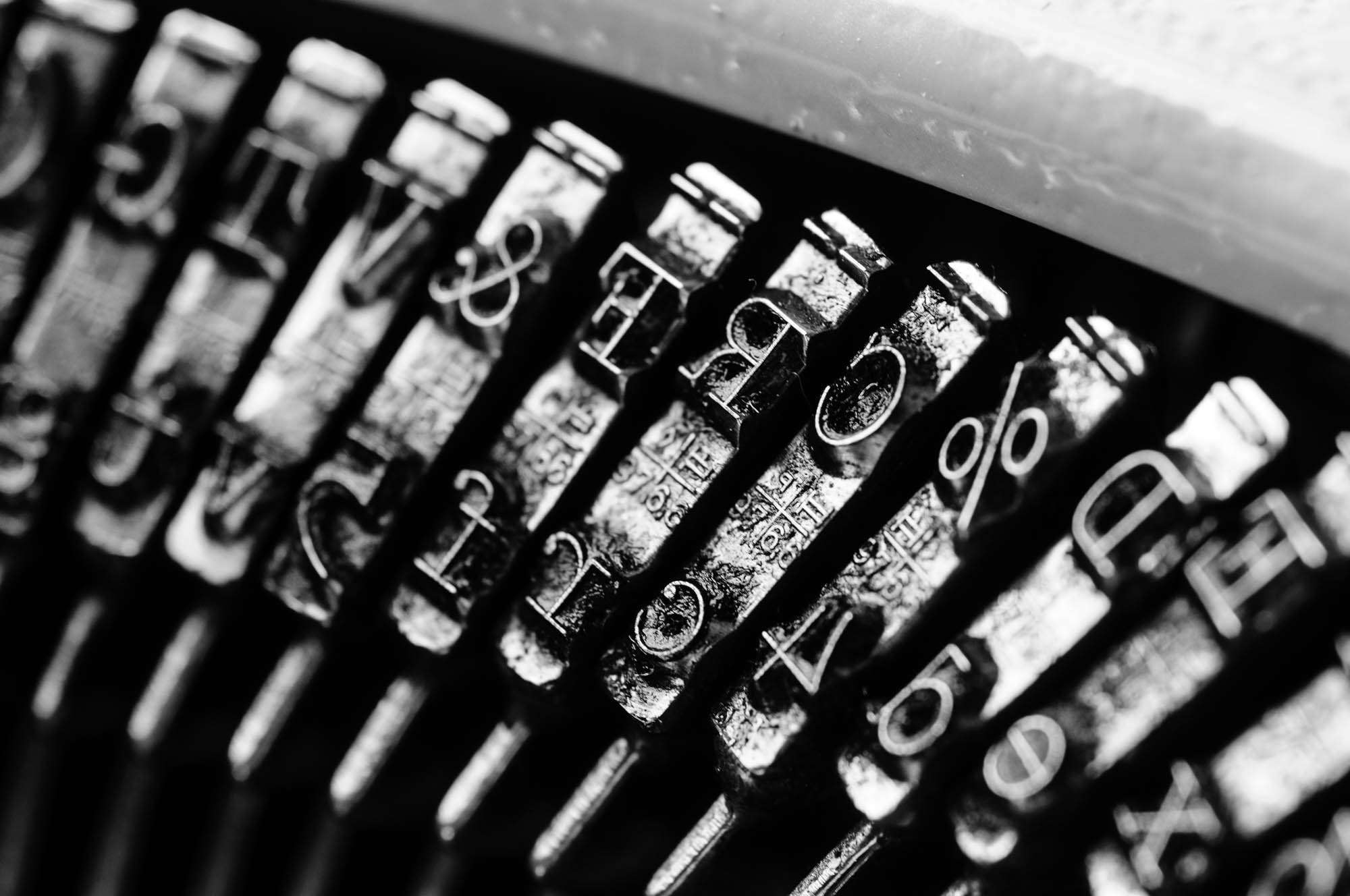 Black and white extreme close-up of typewriter typebars showing characters &, E, B, %, 4, 2, 5, D, A, X, !